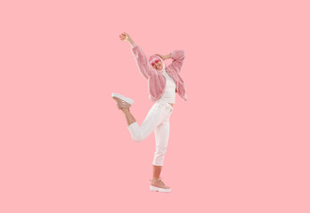 Full length portrait of young happy teenage girl wearing funky clothes and colored wig, dancing and jumping at party, isolated on pink background
