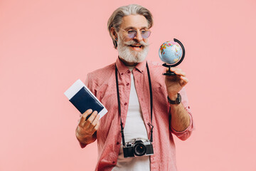 Happy bearded man in sunglasses with a camera and passport chooses a country on a globe for travel.