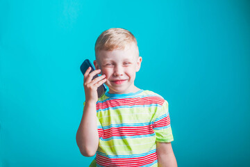 A blond European boy in a striped t-shirt is playing a game on his smartphone. A child makes a pizza order on a mobile phone=. Blue background.