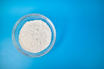 Top view of a bowl full of flour on a blue background with free space for your decoration/text. Concept of having ready for cooking food ingredients.