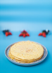 Freshly Made French Crepes/pancakes in a decorative serving plate with icing sugar on the top and summer series on the side one blue background. Concept of perfect breakfast.