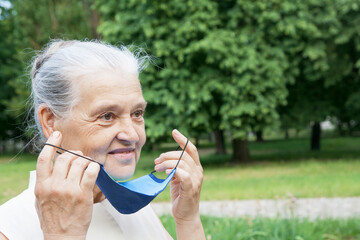 Senior woman dresses or takes off the protective mask outdoors. Virus protection concept for seniors