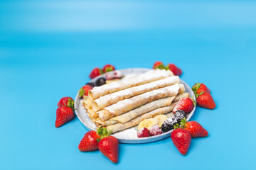 Close-up of a beautifully decorated serving plate full with French Crepes with strawberries around the plate and series inside. Homemade French crepes on blue background with free space for decoration