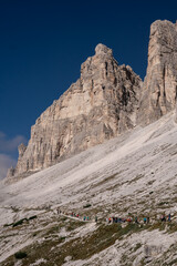 Dolomites Alps. Tre Cime di Lavaredo. Italy. Group of tourists hiking along alpine trail in desert at the foot of the mountain in clear weather on background of blue sky