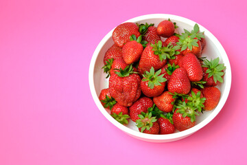 Strawberries are juicy in a bowl. On a pink background.
