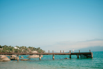Fototapeta na wymiar Foto panorâmica de um pier com um pescador na praia da feiticeira em Ilhabela, litoral norte de são paulo.
