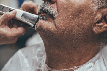 Close up of electric shaver being in hands of a barber.Serious master cutting beard of the aged...
