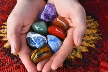 A close up image of a hand holding several chakra crystals over a red table cloth. 