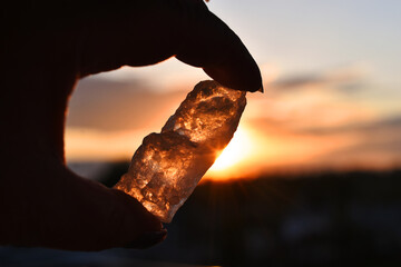 A silhouette image of a clear quartz crystal being held against a orange sunset. 