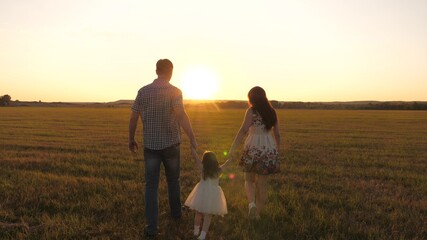 Fototapeta na wymiar little daughter plays and jumps into field holding hands of mom and dad. healthy Happy family with child walks in park at sunset. baby and parent walk in sun. concept of happy family and childhood