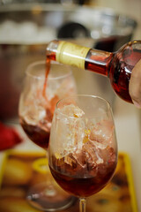 Hand pouring red alcoholic drink in glass with ice