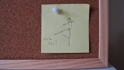 Little drawing of a female doing karate with handwritten inspirational note on a yellow piece of paper sticking to the corner of a pin board 