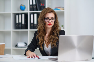 Successful businesswoman at official clothes sitting in cozy bright office and working with laptop computer. Concept of experienced company manager.