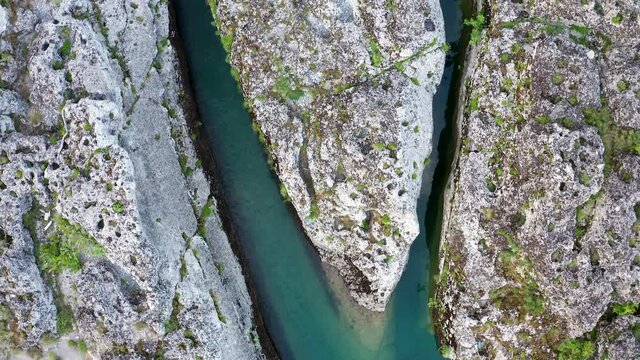 Fork of a green narrow mountain river flowing through rocky landscape. Stream bed cut deep into stones. Upstream of Cijevna (Cem) in Montenegro. Top view aerial footage.