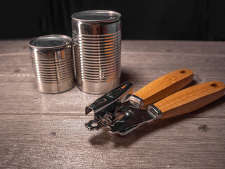 two canned aluminum products with a stainless steel and wooden can opener a wooden board and a black background