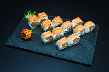 Sushi, traditional Japanese cuisine. Delicious Uramaki on decorated plate, black background.