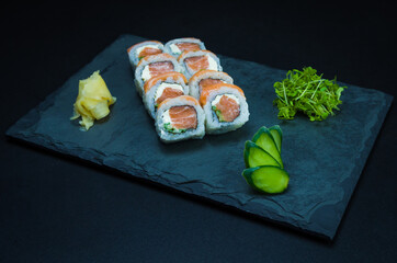 Sushi, traditional Japanese cuisine. Delicious Uramaki on decorated plate, black background.