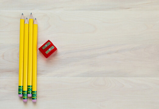 4 yellow pencils lined up next to a red pencil sharpener on a wood background with copy space