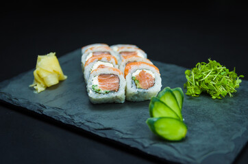 Sushi, traditional Japanese cuisine. Delicious Uramaki on decorated plate, black background.
