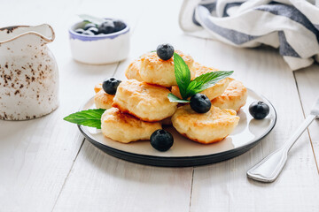 Trandy food - fluffy mini pancakes with blueberries and mint on a white wooden background.