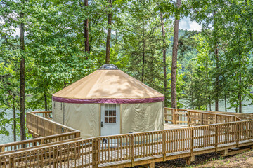 A YURT on a wooden deck in a forest camp ground.