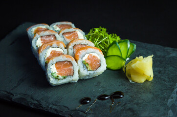 Sushi, traditional Japanese cuisine. Delicious Uramaki on decorated plate, black background.