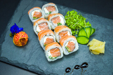 Sushi, traditional Japanese cuisine. Delicious Uramaki on decorated plate, black background.