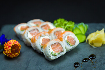 Sushi, traditional Japanese cuisine. Delicious Uramaki on decorated plate, black background.