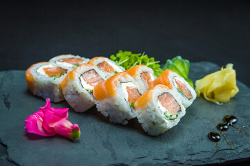 Sushi, traditional Japanese cuisine. Delicious Uramaki on decorated plate, black background.