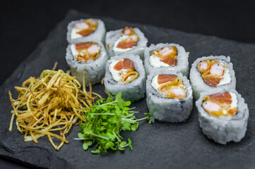 Sushi, traditional Japanese cuisine. Delicious Uramaki on decorated plate, black background.