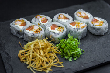 Sushi, traditional Japanese cuisine. Delicious Uramaki on decorated plate, black background.