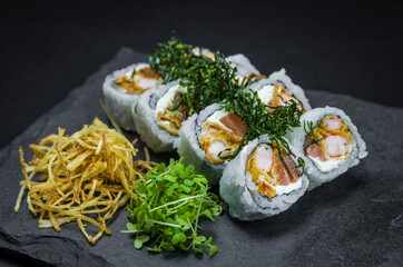 Sushi, traditional Japanese cuisine. Delicious Uramaki on decorated plate, black background.