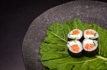Sushi, traditional Japanese cuisine. Delicious hossomaki on the decorated plate, black background.