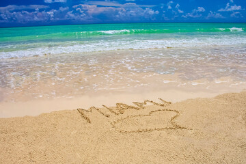Tropical beach in Miami with bright blue sky, turquoise water and Miami written on the sand