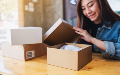  A beautiful young asian woman receiving and opening a postal parcel box at home for delivery and online shopping concept
