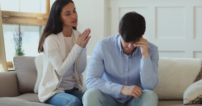 Young guilty mixed race wife folded hands in namaste, begging apologizing to offended husband, feeling stressed after misunderstanding. Woman asking forgiveness to displeased boyfriends at home.