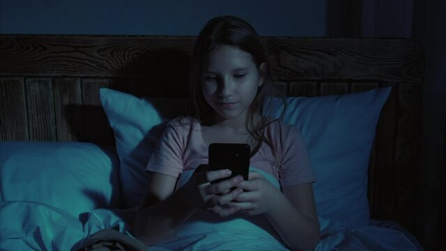 Teen leisure. Night online chat. Girl using smartphone for texting in bed before sleep.