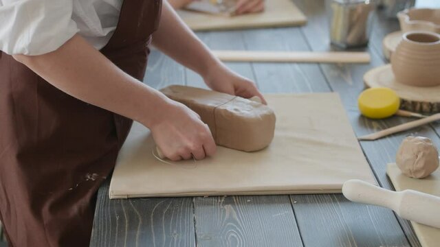 Female potter cutting piece of pottery clay using trimming tool close-up. Woman use clay cutter to a raw piece of clay