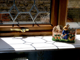 sunlight falls on the window sill through a delicately glazed window, a ceramic figure of a garden-caring hare stands on the windowsill