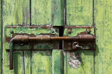 Rustic green and rusty hasp holding an old wooden door