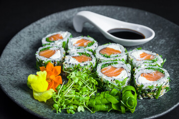 Perfect sushi, traditional Japanese cuisine. Delicious uramaki with shoyo sauce on the decorated plate, black background.
