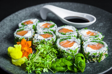 Perfect sushi, traditional Japanese cuisine. Delicious uramaki with shoyo sauce on the decorated plate, black background.