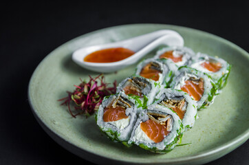 Perfect sushi, traditional Japanese cuisine. Delicious uramaki with sweet and sour sauce on the decorated plate, black background.