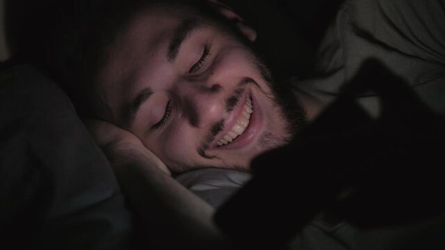 Bedtime movie. Sleepless night. Man enjoying watching comedy video on phone laughing.