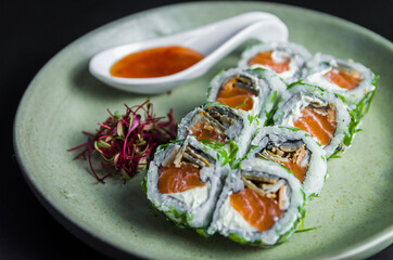 Perfect sushi, traditional Japanese cuisine. Delicious uramaki with sweet and sour sauce on the decorated plate, black background.