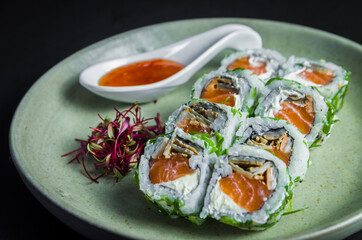 Perfect sushi, traditional Japanese cuisine. Delicious uramaki with sweet and sour sauce on the decorated plate, black background.