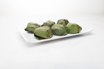 Koci the malaysian glutinous rice ball served in banana leaf on white plate over wooden table