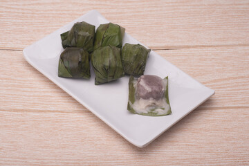 Koci the malaysian glutinous rice ball served in banana leaf on white plate over wooden table