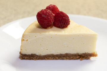 A creamy cheesecake topped with fresh raspberries on a white plate waiting to be served.