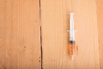 A syringe filled with orange liquid isolated over cream color wooden background